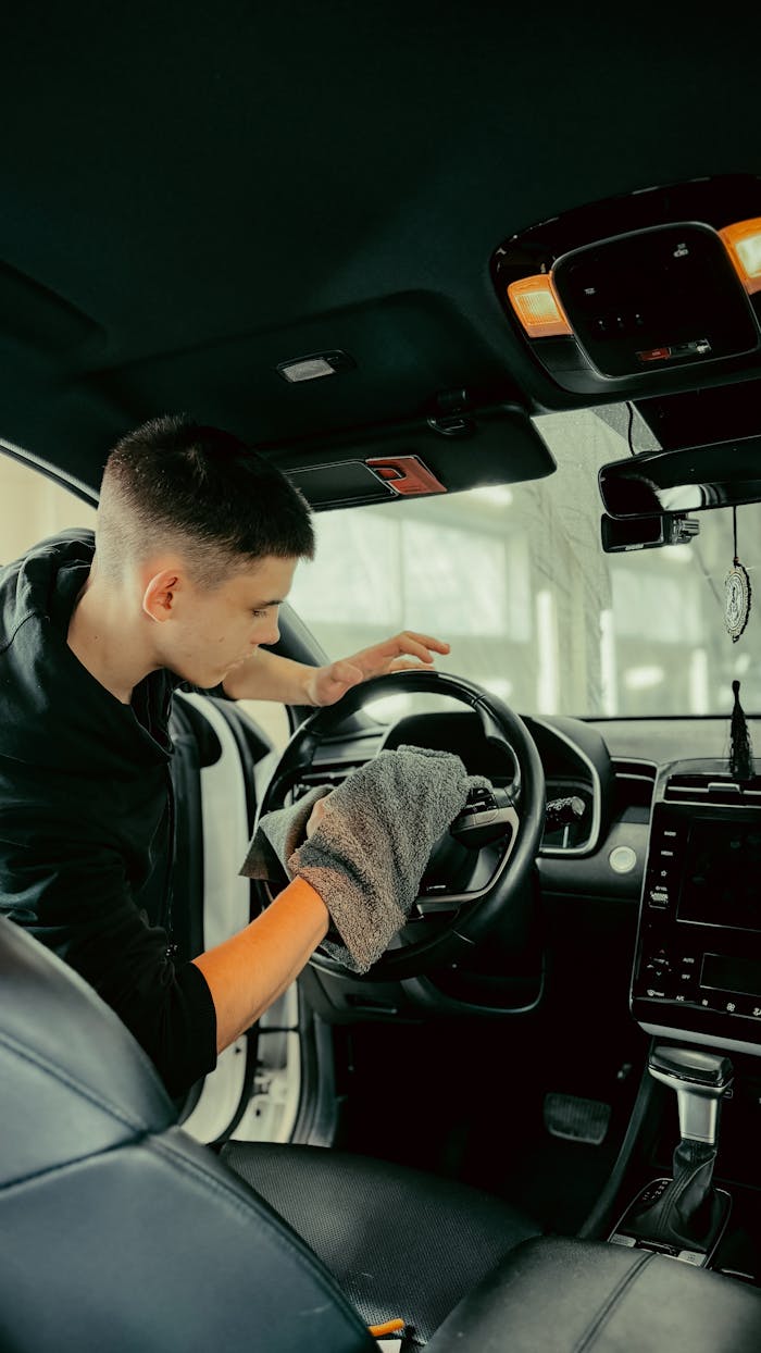 Young man polishing car steering wheel with cloth, ensuring clean interior.