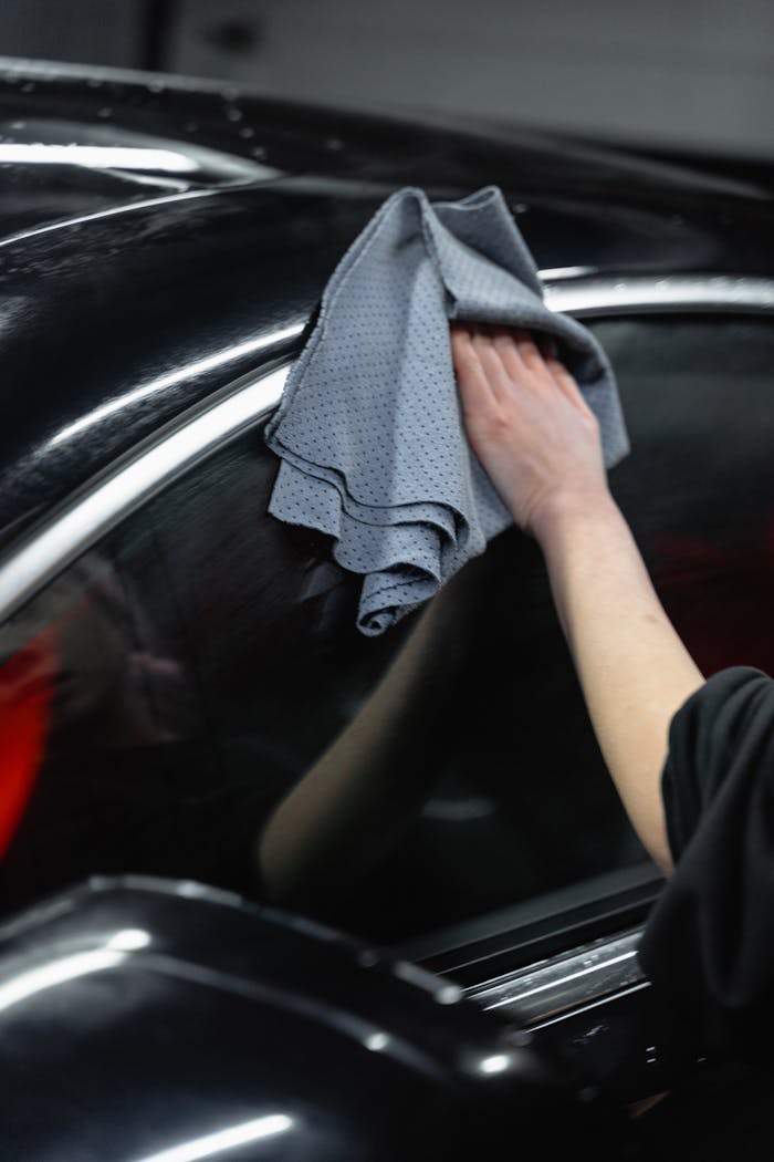 Hand cleaning black car exterior with cloth, showcasing car care and detailing.