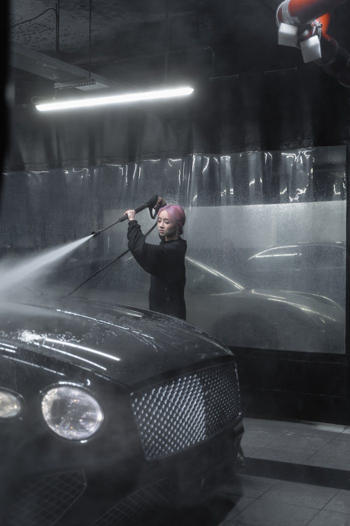 A professional female cleaner power washing a luxury car in a modern garage.